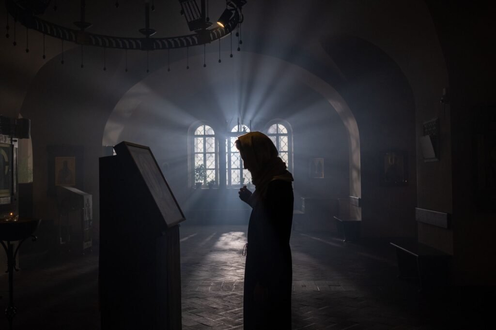 A contemplative woman praying by a window, seeking God's presence during lonely moments